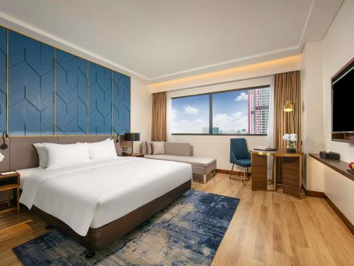 ハノイにあるMövenpick Living West Hanoiの大きなベッドと机があるホテルの部屋