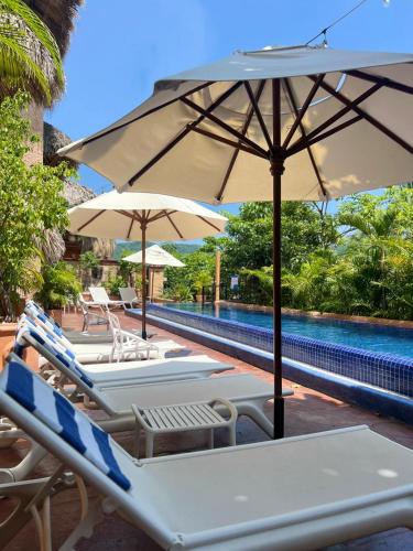 a group of lounge chairs and umbrellas next to a pool at Ensueño de Fuga in Zihuatanejo
