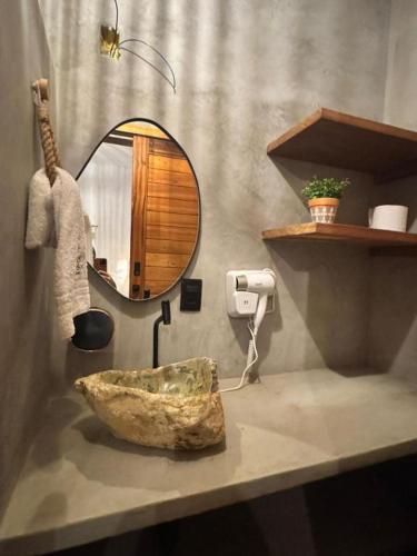 a bathroom with a mirror and a stone bowl on a counter at Maré Mansa Suítes Icaraizinho in Amontada
