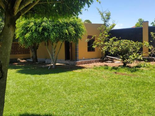 a yellow house with a yard with grass and trees at Gipir & Labango Ventures in Entebbe