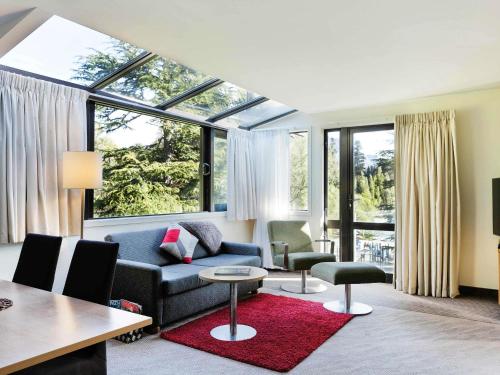 a living room with a couch and chairs and windows at Novotel Queenstown Lakeside in Queenstown