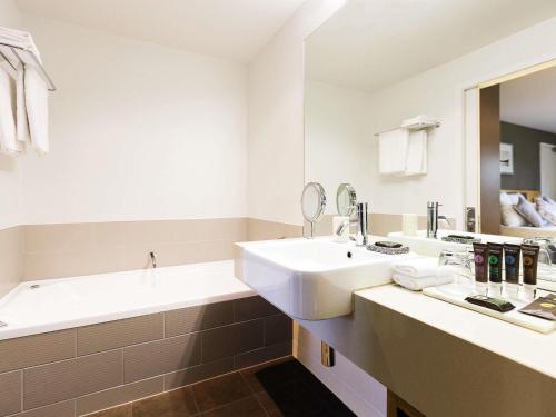 a white bathroom with a sink and a tub at Novotel Queenstown Lakeside in Queenstown