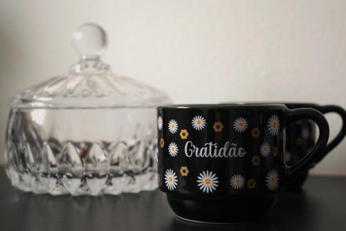 a black cup with flowers on it next to a glass container at Apartamento dalias em Holambra in Holambra
