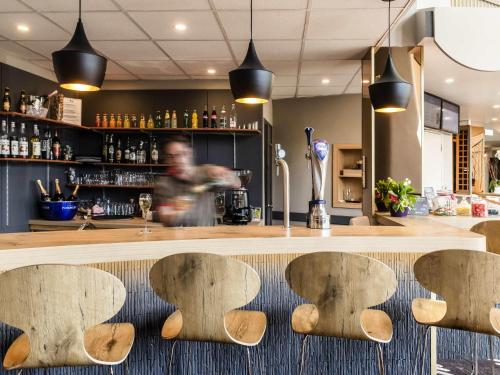 a bar with a person walking behind a counter at Ibis Château-Thierry in Essômes-sur-Marne