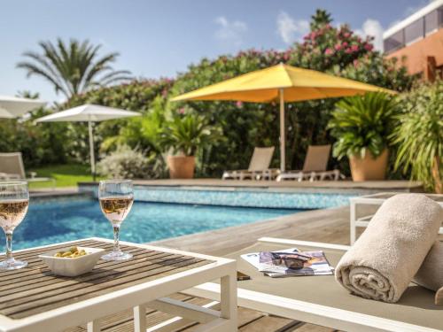 a table with glasses of wine next to a pool at Mercure Hyères Centre Côte d'Azur in Hyères