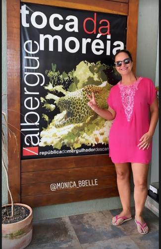 a woman in a pink dress standing in front of a sign at Hostel Toca da Moréia Bombinhas in Bombinhas
