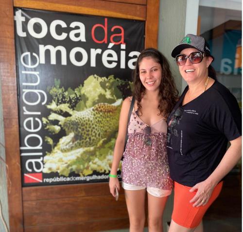 two women are standing in front of a sign at Hostel Toca da Moréia Bombinhas in Bombinhas