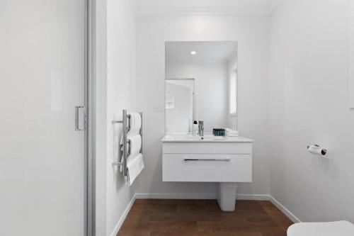 a white bathroom with a sink and a mirror at Perfect Papamoa Beach Bach in Papamoa