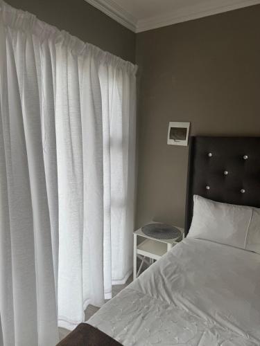 una camera da letto con un letto e una finestra con tende bianche di Room in Cimbebasia a Windhoek