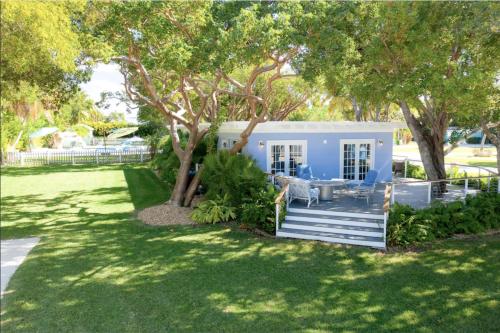 a blue house with a porch and trees at Charming Bayfront Cottage in Heart of Islamorada with Pool, Dockage, Beach, Kayaks & More in Islamorada