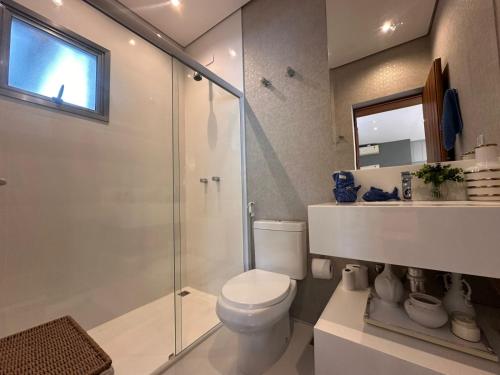 a bathroom with a toilet and a glass shower at Casa Alto Padrão - Riviera de São Lourenço in Bertioga
