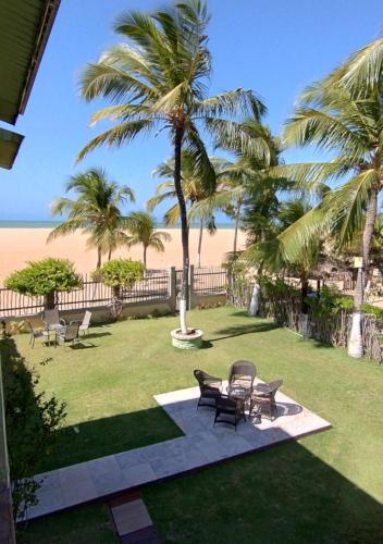 a patio with chairs and a table and palm trees at Pousada Chantilly in São Miguel do Gostoso