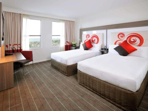 a hotel room with two beds and a desk at Novotel Melbourne Glen Waverley in Glen Waverley