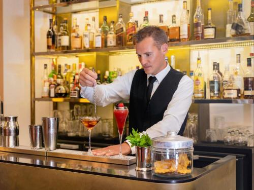 a bartender making a drink at a bar at Carlton Hotel Lyon - MGallery Collection in Lyon