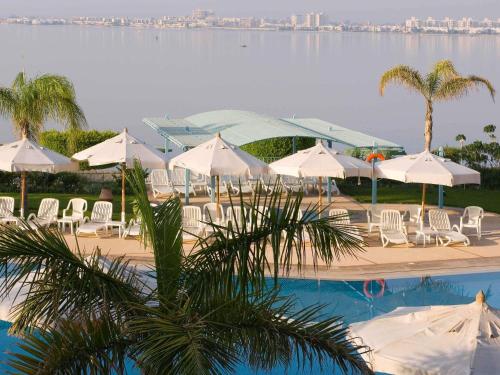 a pool with white umbrellas and chairs and a body of water at Mercure Ismailia Forsan Island in Ismailia
