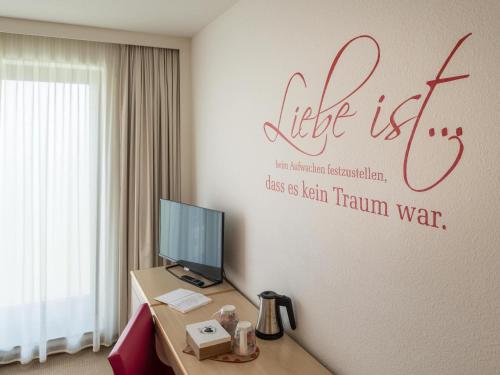 a room with a desk with a computer and a sign on the wall at Novotel Berlin Mitte in Berlin