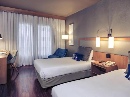 a hotel room with two beds and a chair at Mercure Campinas in Campinas