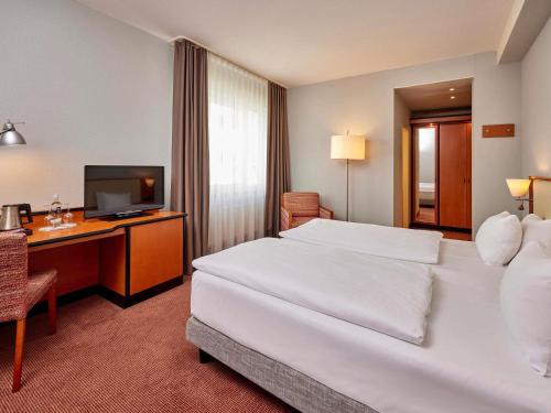 a hotel room with a bed and a desk with a television at Mercure Hotel Düsseldorf City Center in Düsseldorf