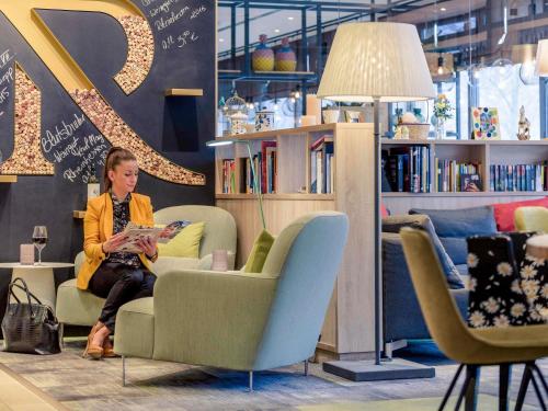 a woman sitting in a chair reading a book at Mercure Hotel Hannover Mitte in Hannover