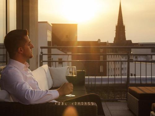 a man sitting on a balcony with a glass of wine at Mercure Hotel Hannover Mitte in Hannover