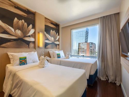 two beds in a hotel room with a window at Mercure Manaus in Manaus