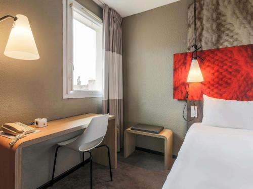 a hotel room with a bed and a desk and a bed and a window at Ibis Albi in Albi
