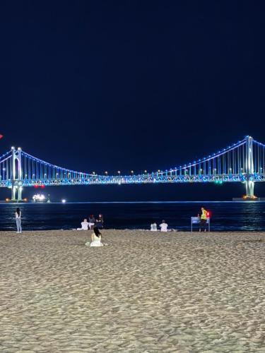 a bridge over the water at night with people on the beach at Seaside Mood 2BR near Gwangalli in Busan