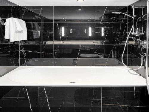 a bath tub in a black tiled bathroom at Sofitel London Gatwick in Horley