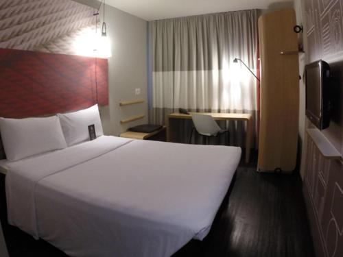 a hotel room with a large white bed and a desk at ibis Navegantes Itajai in Itajaí