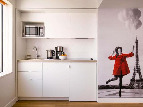 a kitchen with white cabinets and a mural of a woman jumping at Aparthotel Adagio Paris Centre Tour Eiffel in Paris