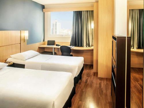 a hotel room with two beds and a desk at Ibis Belo Horizonte Savassi in Belo Horizonte
