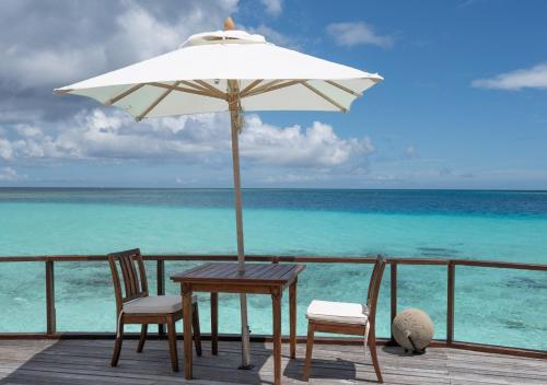 a table and two chairs and an umbrella on a deck at Makunudu Island- An Intimate Hideaway in Makunudhoo