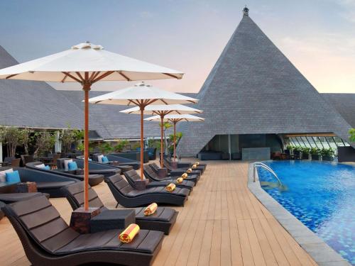 szereg leżaków i parasoli przy basenie w obiekcie The Kuta Beach Heritage Hotel - Managed by Accor w mieście Kuta