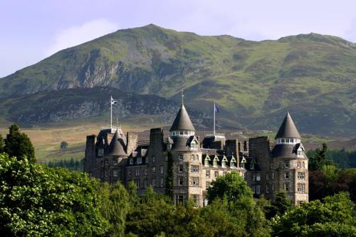 a castle on a hill with a mountain in the background at Lodges by Atholl Palace in Pitlochry