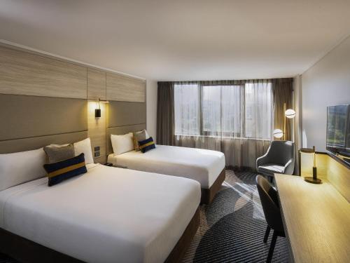 a hotel room with two beds and a desk at Novotel Sydney Parramatta in Sydney