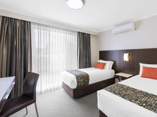 a hotel room with two beds and a desk at Mercure Wagga Wagga in Wagga Wagga