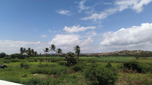 a field with palm trees and a sky with clouds at NANDANAVANA Homestay in New Hampi