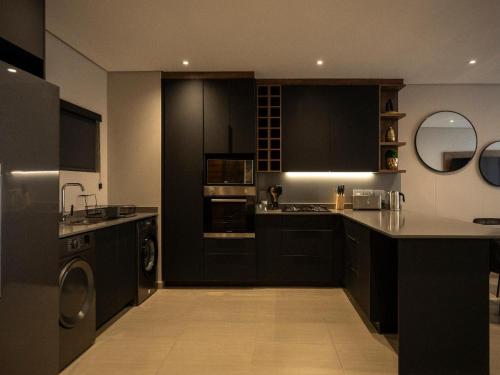 a kitchen with black cabinets and a washer and dryer at Lux Leisure Apartment Hotel Sandton in Johannesburg