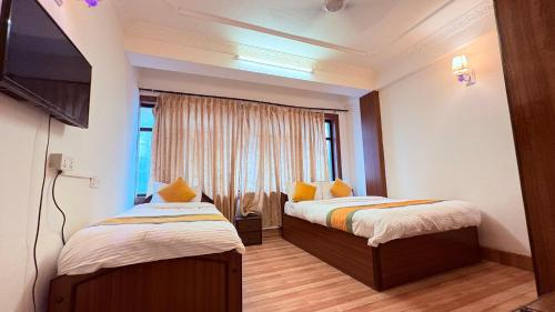 Un dormitorio con dos camas y un televisor y una ventana. en Hotel Divine Inn, en Katmandú