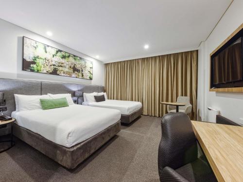 a hotel room with two beds and a desk at Mercure Penrith in Penrith