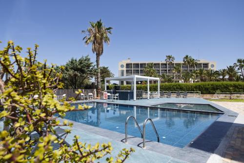 a swimming pool with a palm tree and a building at Naiades Hotel by Estia in Kato Gouves