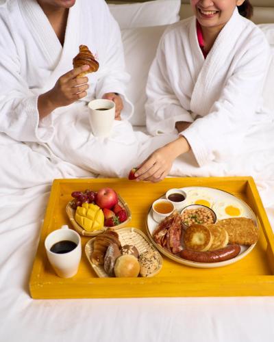 麦克坦Savoy Hotel Mactan Cebu near Newtown Beach的坐在床上的男人和女人,拿着一盘食物