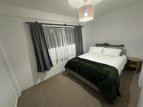 a bedroom with a bed with a green blanket and a window at Across The Dunes, Papamoa in Papamoa