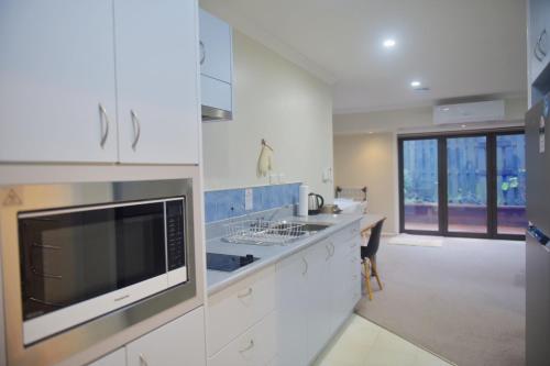 a white kitchen with a sink and a microwave at Family Friendly 1BR in Howick, Near Beach and Cafes in Auckland