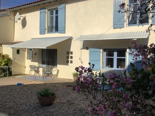een wit huis met blauwe ramen en een patio bij Les Jonquilles in Chef-Boutonne