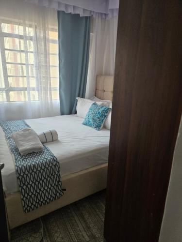 a bed with blue and white pillows and a window at Hami Ventures in Kisumu