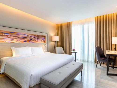 a bedroom with a large white bed and a desk at Novotel Phuket City Phokeethra in Phuket Town