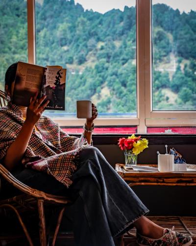 a woman sitting in a chair reading a book at Aurevelle Kastura Resort Kanatal - Mountain View Rooms in Kanatal