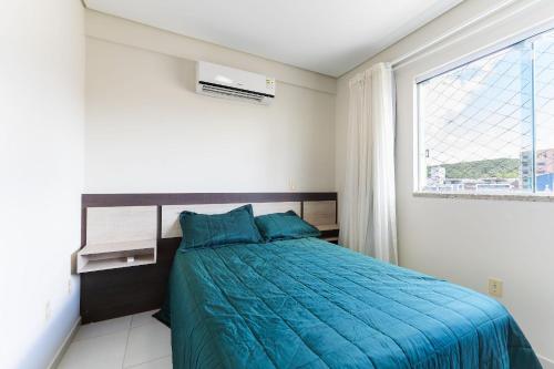 a bedroom with a bed with a blue comforter and a window at Res. Wilian 308 - Apto 2 quartos em Bombas in Bombas