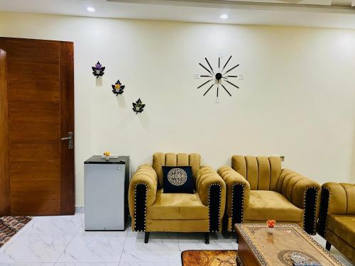 a living room with two chairs and a clock on the wall at 1 bed furnished apartment flat Bahria town Rwp isb in Rawalpindi